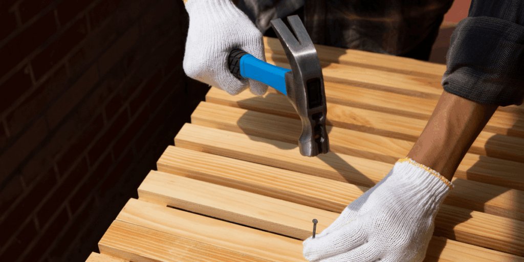 A person wearing gloves uses a hammer to cut a piece of wood on a workbench.