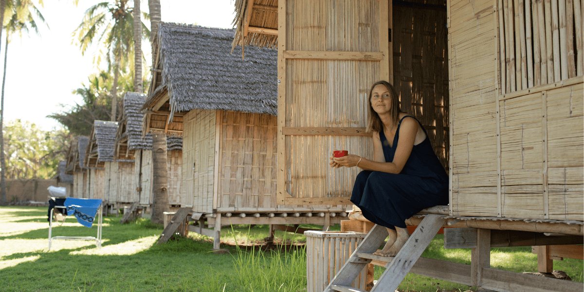 A woman seated on a wooden deck in front of a hut, enjoying the outdoor scenery.